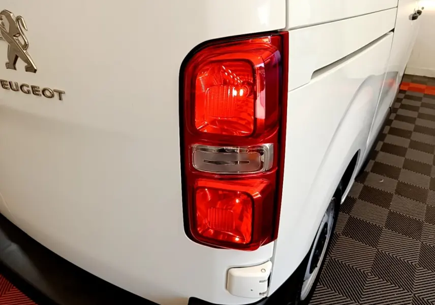 Gros plan sur le feu arrière droit d’un Peugeot Traveller blanc de 2018, avec logo et partie latérale visible.