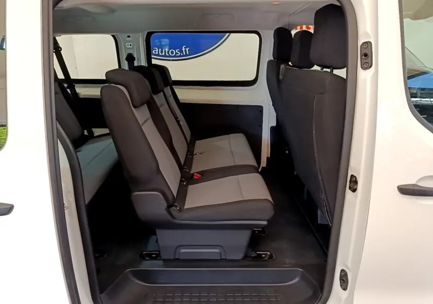 Vue latérale intérieure du Peugeot Traveller blanc 2018 montrant la rangée de sièges en tissu gris et noir.