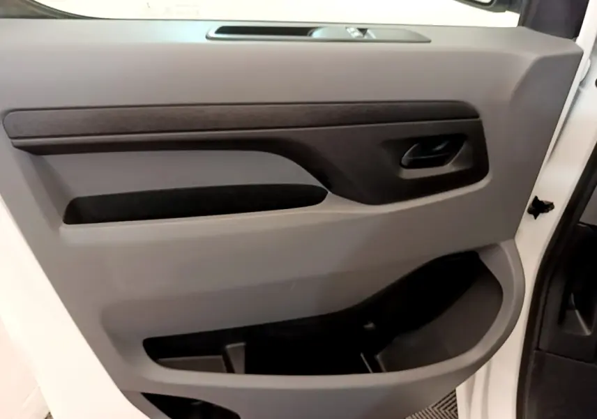 Vue intérieure du panneau de porte avant gauche du Peugeot Traveller blanc, avec poignée noire et rangements intégrés.