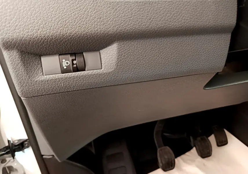 Détail intérieur côté gauche du Peugeot Traveller blanc 2018 montrant le réglage des phares et les trois pédales manuelles.