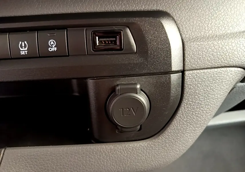 Gros plan sur la console centrale noire du Peugeot Traveller 2018, montrant prise 12V, port USB et boutons de contrôle.