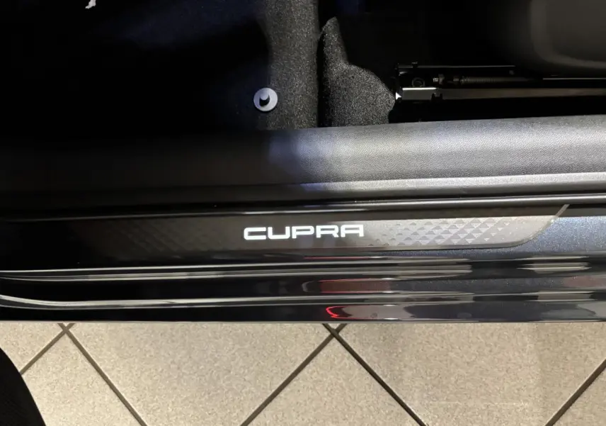 Gros plan sur le seuil de porte noir brillant avec logo CUPRA blanc, intérieur suédine noire visible en arrière-plan.