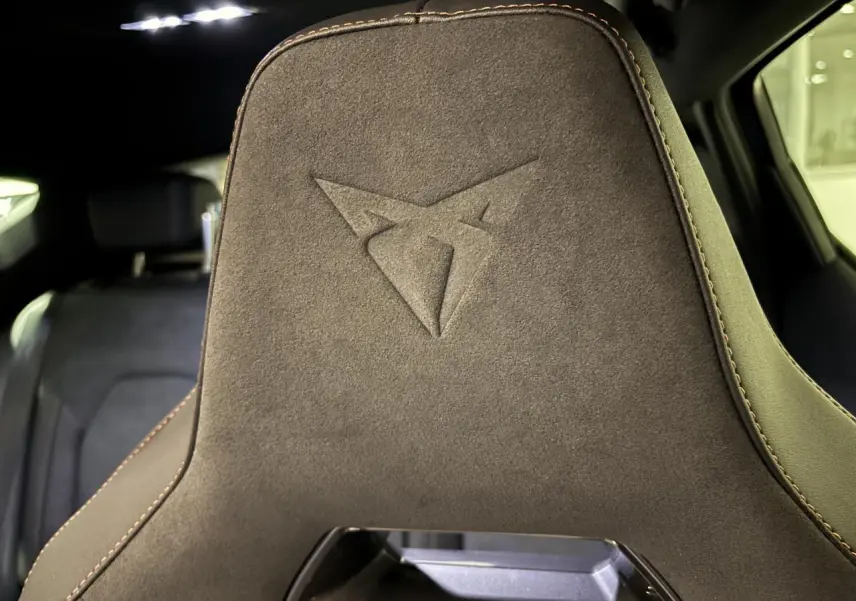 Gros plan sur le dossier avant en suédine noire avec logo Cupra embossé et surpiqûres cuivrées dans l’habitacle.