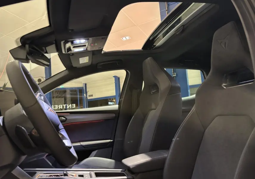 Intérieur CUPRA Leon 2026 vu côté gauche, sièges baquets noirs et toit ouvrant panoramique visible.