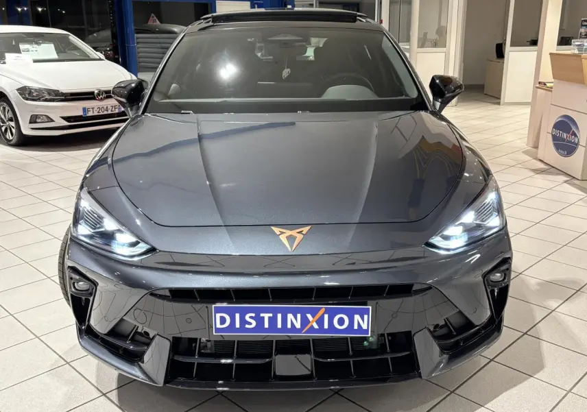 Vue avant d'une CUPRA Leon gris Graphène avec logo cuivré et phares LED allumés en showroom.