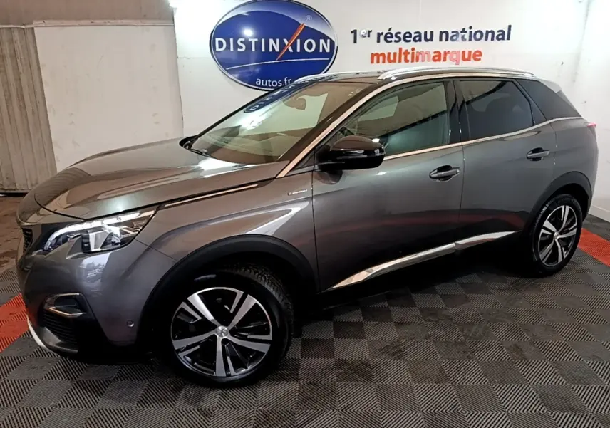 Peugeot 3008 gris foncé en vue 3/4 avant droit, avec jantes alliage et feux LED allumés, stationné en intérieur.