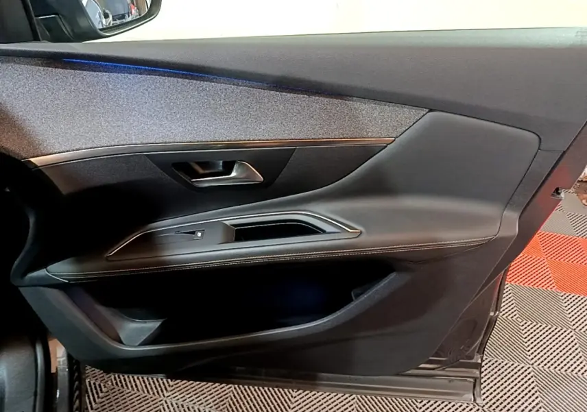 Vue intérieure côté gauche de la porte avant d’un Peugeot 3008 gris foncé avec garniture noire et surpiqûres blanches.