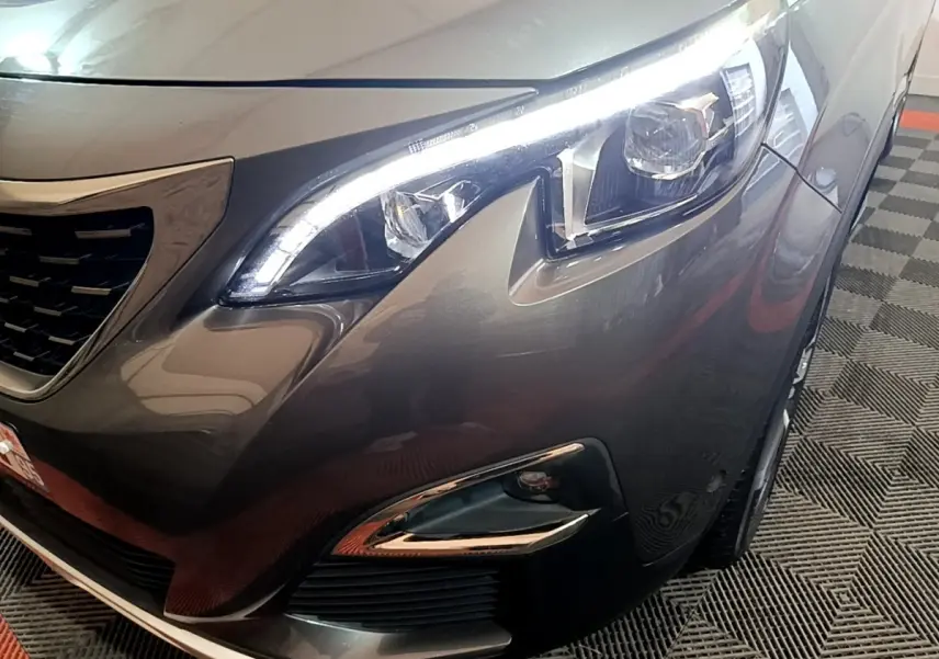 Gros plan sur l'avant droit gris foncé du Peugeot 3008, mettant en valeur le phare LED et la calandre distinctive.