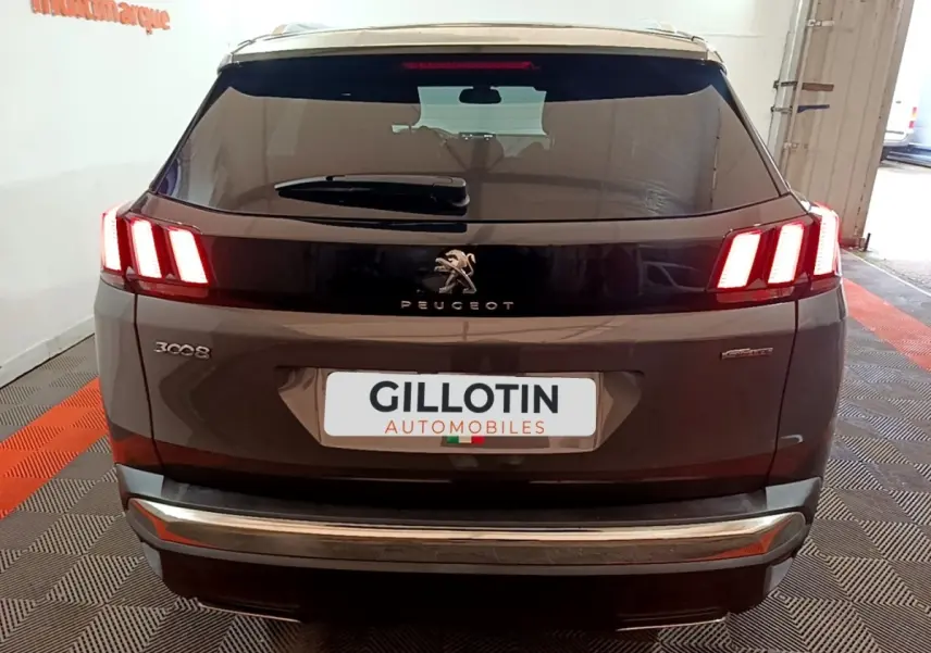 Vue arrière d'un Peugeot 3008 gris foncé avec feux LED allumés et logo Peugeot visible sur hayon noir brillant.