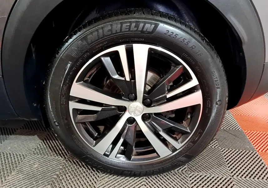 Gros plan sur la roue avant droite du Peugeot 3008 gris foncé, jante alliage bicolore et pneu Michelin visible.