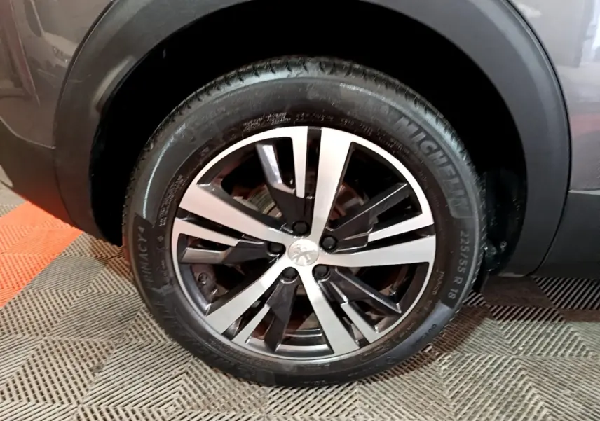 Gros plan sur la roue avant droite du Peugeot 3008 gris foncé, mettant en valeur la jante alliage bicolore.