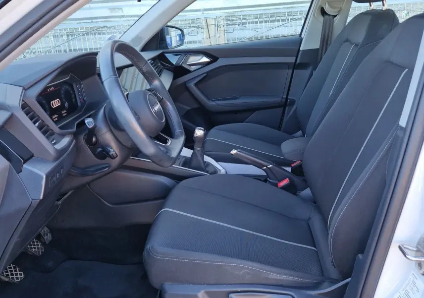 Vue intérieure côté conducteur de l'Audi A1 Sportback blanc glacier 2020 avec sièges noirs et volant multifonction.