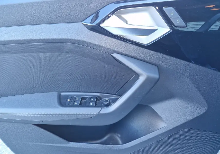 Détail de la porte côté conducteur noire de l'Audi A1 Sportback 25 TFSI 2020 avec commandes des vitres et poignée argentée.