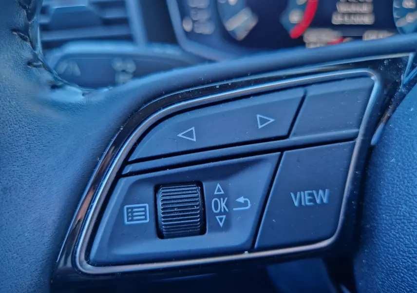 Gros plan sur les commandes multifonctions noires du volant d'un Audi A1 Sportback blanc glacier, avec boutons fléchés et "VIEW".