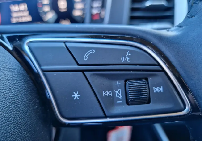 Gros plan sur les commandes multifonctions noires du volant d’un Audi A1 Sportback blanc glacier, avec boutons d’appel et volume.