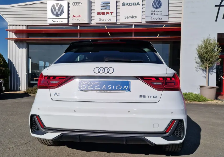 Vue arrière d'une Audi A1 Sportback blanc glacier 2020 avec feux LED et logo distinctif sur un parking de concession.