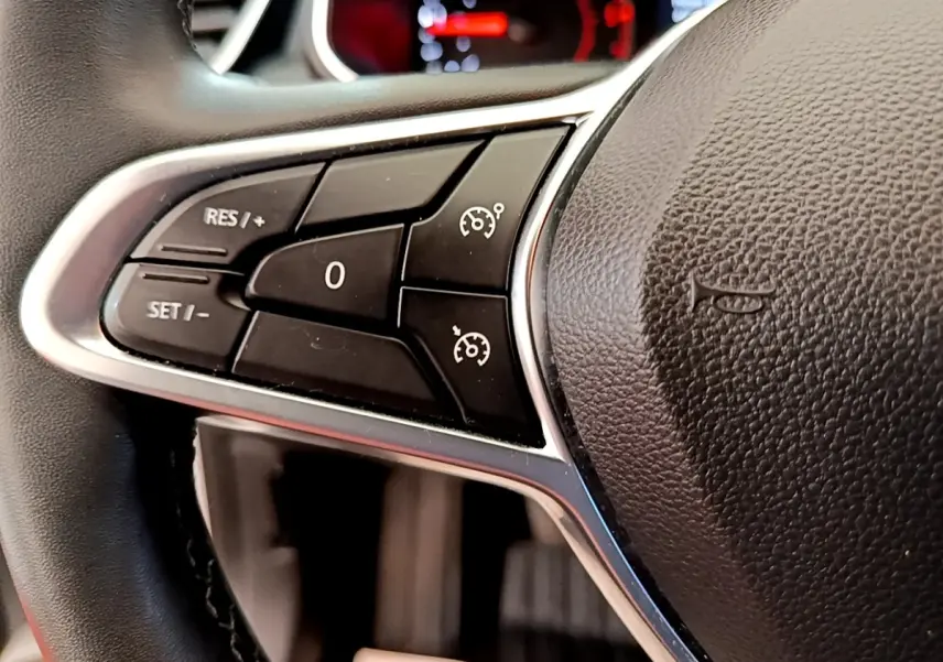 Gros plan sur les commandes de régulateur de vitesse à gauche du volant noir d'une Renault Clio Business Blue dCi 85 blanche.