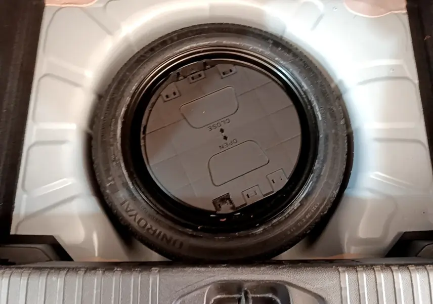 Vue plongeante sur la roue de secours noire dans le coffre blanc d'une Renault Clio Business Blue dCi 85 2020.