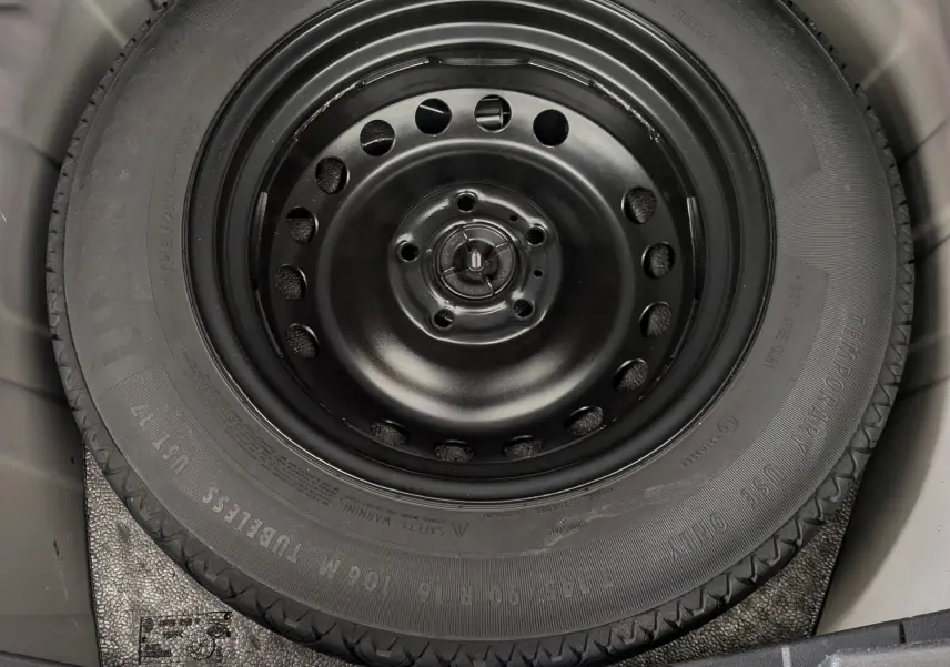 Roue de secours noire montée sur jante acier, vue en plongée dans le coffre d’un Nissan Juke rouge 2020.