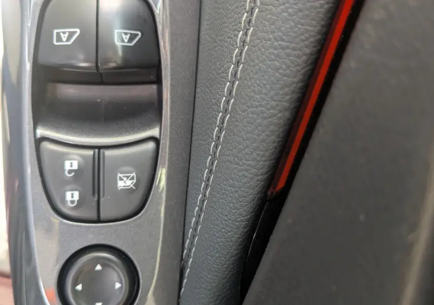 Détail des commandes de lève-vitres et rétroviseurs sur la portière côté conducteur d’un Nissan Juke rouge 2020.