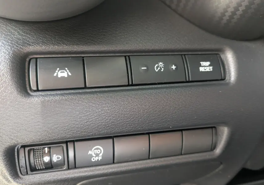 Détail des commandes du tableau de bord noir du Nissan Juke rouge 2020, avec régulateur de vitesse et réglage des phares.