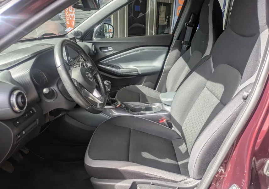 Vue intérieure côté conducteur du Nissan Juke rouge 2020, mettant en valeur le volant cuir et la boîte manuelle.