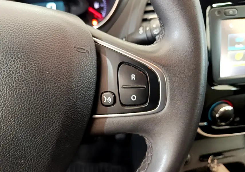 Gros plan sur le volant cuir du Renault Captur Business gris foncé, avec commandes vocales et écran tactile visible en arrière-plan.