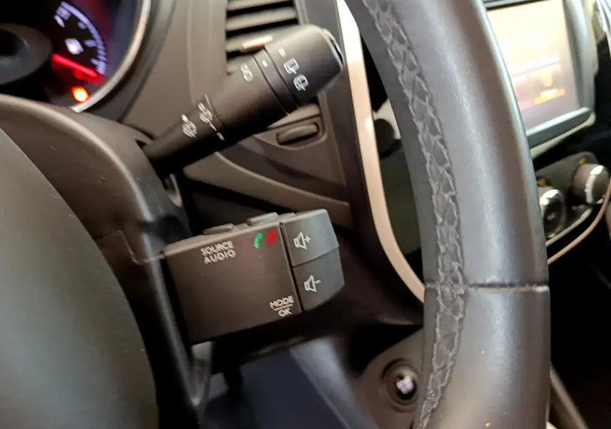 Gros plan sur la commande audio au volant cuir du Renault Captur gris foncé, avec tableau de bord et écran tactile en arrière-plan.