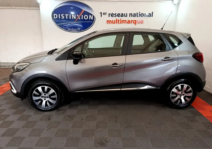 Profil côté gauche d'un Renault Captur Business gris foncé 2018 dans un showroom avec logo Distinxion en arrière-plan.