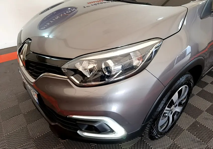 Gros plan sur l'avant droit du Renault Captur gris foncé 2018, mettant en valeur son phare et sa calandre distinctive.
