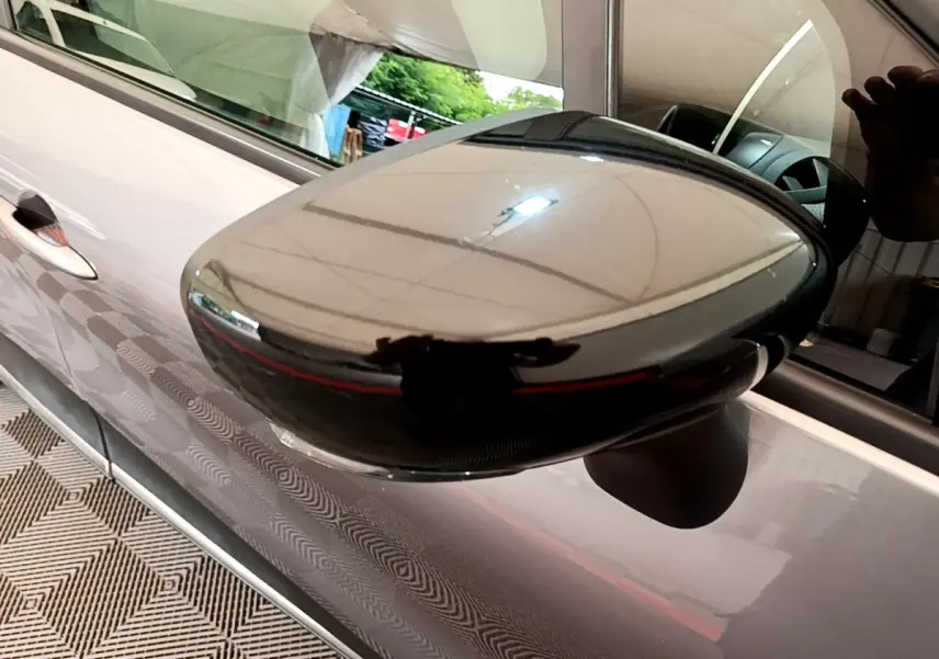 Gros plan sur le rétroviseur droit noir brillant du Renault Captur gris foncé, reflet de l'environnement intérieur visible.