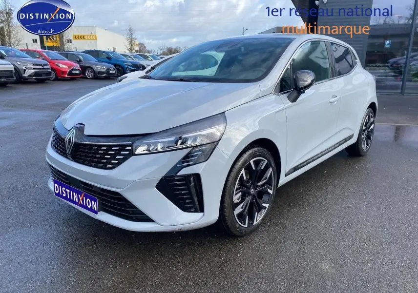 Vue 3/4 avant d'une Renault Clio V gris rafale avec jantes alliage noires et calandre chromée sur parking humide.