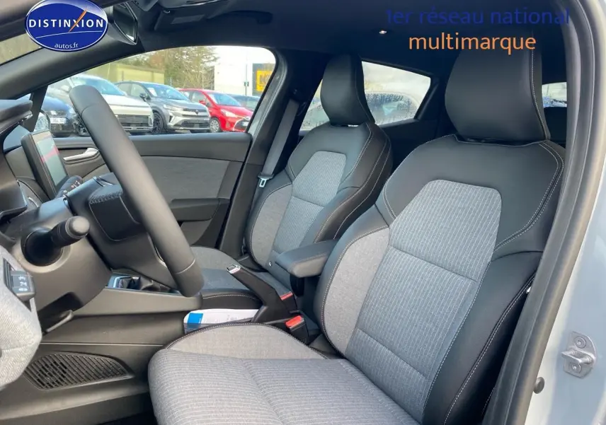 Vue intérieure côté conducteur de la Renault Clio V gris rafale, montrant les sièges tissu et cuir avec accoudoir central.