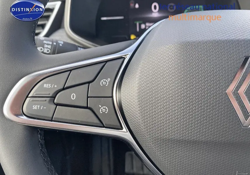 Gros plan sur le volant multifonction gris avec commandes de régulateur de vitesse et logo Renault visible.