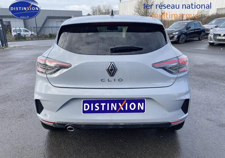 Vue arrière d'une Renault Clio V gris rafale avec feux LED et sortie d'échappement chromée sur parking humide.