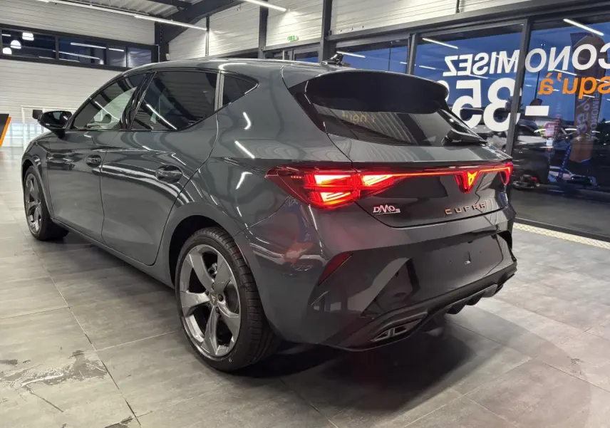 Vue 3/4 arrière droite de la CUPRA Leon 2026 en bleu Fjord avec feux arrière allumés et jantes alliage 18 pouces.