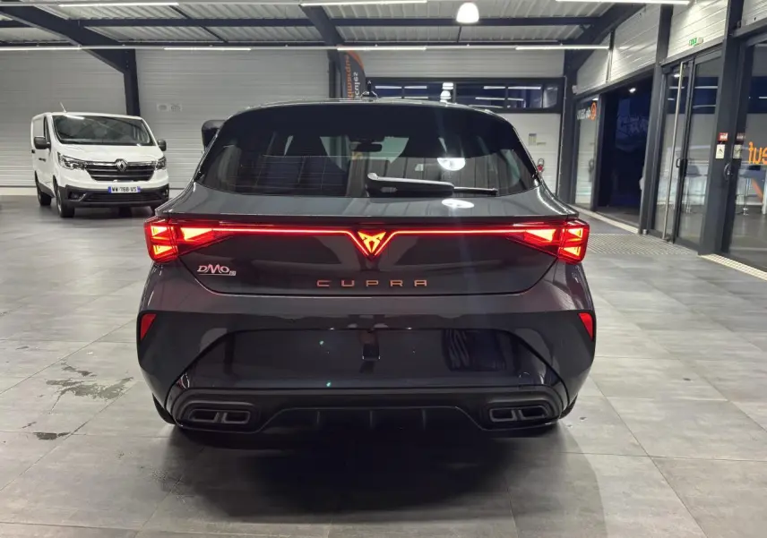 Vue arrière d'une CUPRA Leon bleu Fjord avec feux arrière Tri-LED et double sortie d'échappement noire en intérieur showroom.