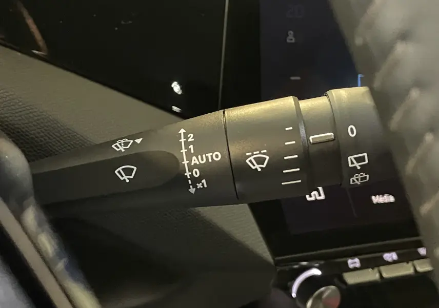 Gros plan sur la commande d’essuie-glace à gauche du volant dans l’habitacle sombre d’une Peugeot 308 Hybrid 2025.