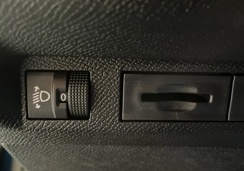 Gros plan sur le réglage de hauteur des phares dans l'habitacle d'une Peugeot 308 Hybrid 2025, surface noire texturée.