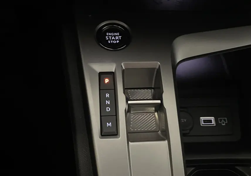 Gros plan sur la console centrale grise de la Peugeot 308 Hybrid 145, montrant le bouton start/stop et la commande de boîte automatique.