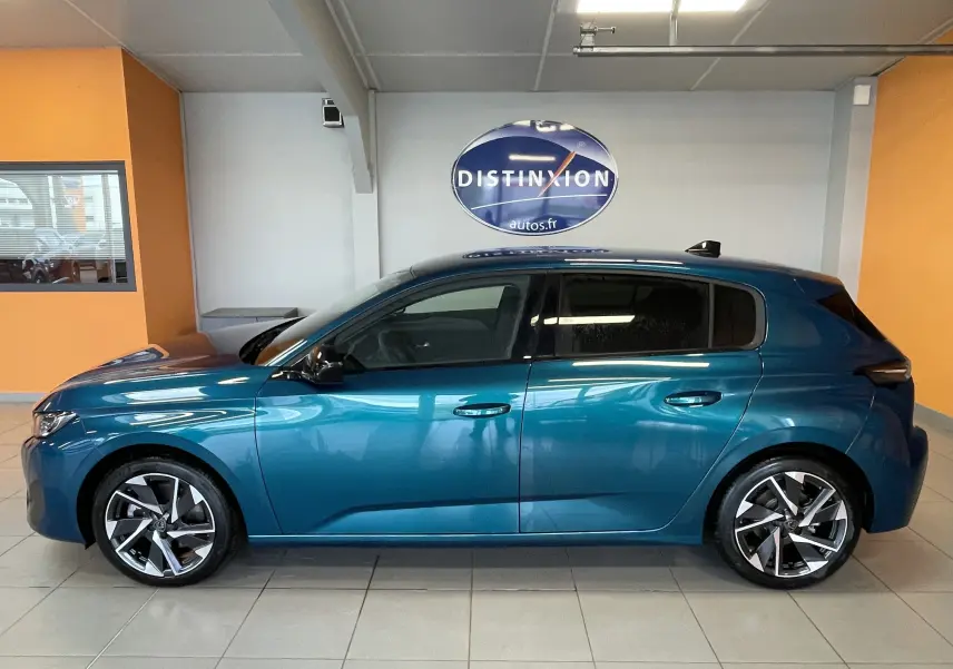 Profil latéral droit de la Peugeot 308 Hybrid 145 Allure en bleu obsession, avec jantes alliage 17 pouces dans un showroom.