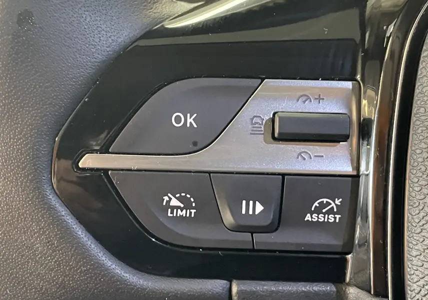 Gros plan sur les commandes au volant de la Peugeot 308 Hybrid 145, boutons noirs avec marquages blancs.