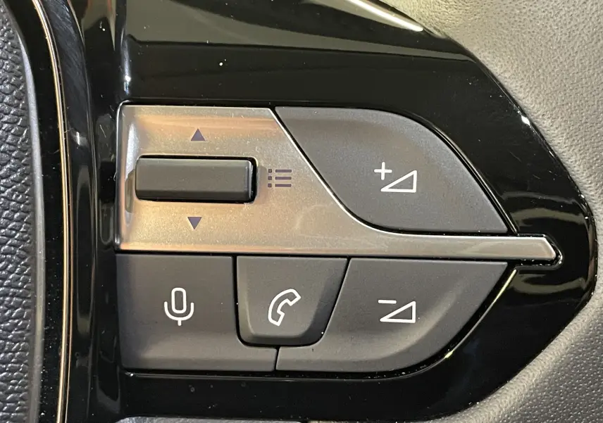 Gros plan sur les commandes multifonctions noires du volant de la Peugeot 308 Hybrid 145 e-DCS6 Allure, finition 2025.