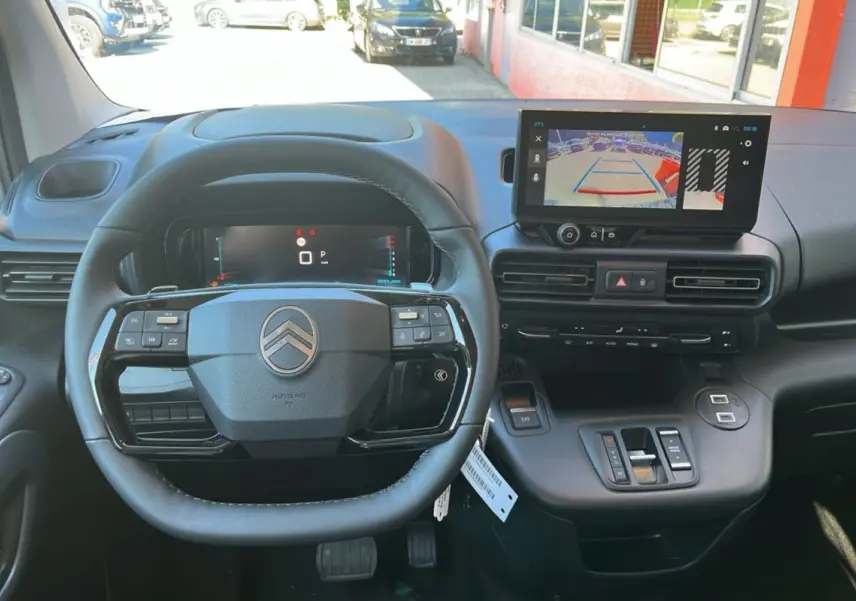 Vue intérieure centrée sur le volant cuir multifonctions et l'écran tactile affichant la caméra de recul du Citroën Berlingo noir.