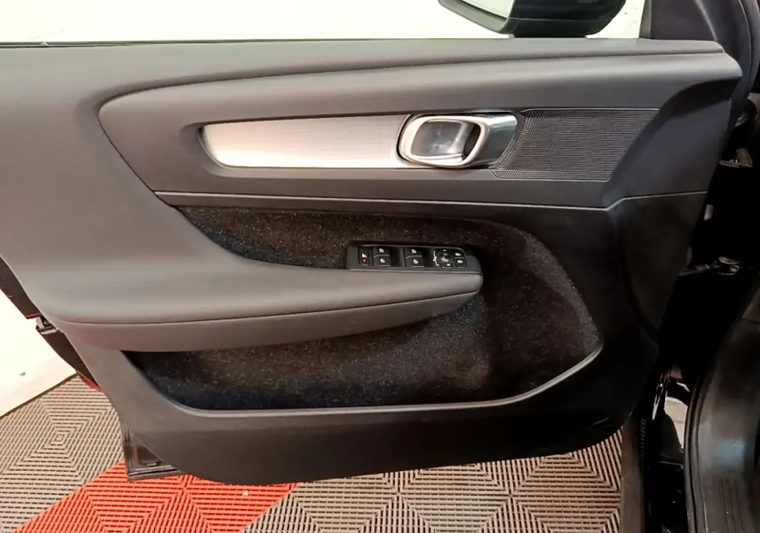 Vue intérieure côté gauche de la porte avant noire du Volvo XC40 T2 Momentum avec commandes de vitres et poignée chromée.