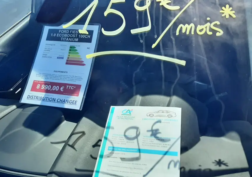 Vue intérieure du pare-brise d'une Ford Fiesta marron métal 2013 avec affichage du prix et mensualité en jaune.