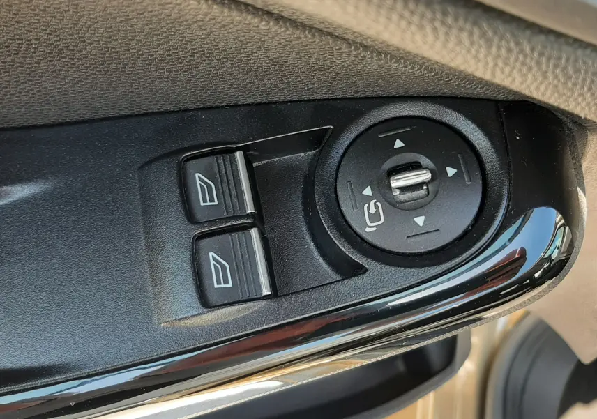 Gros plan sur les commandes de réglage des rétroviseurs et des vitres côté conducteur d'une Ford Fiesta marron métal 2013.