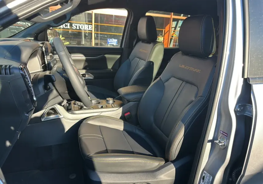 Vue intérieure côté conducteur du Ford Ranger 2025 gris iconic, sièges en cuir noirs avec surpiqûres jaunes et logo Wildtrak brodé.