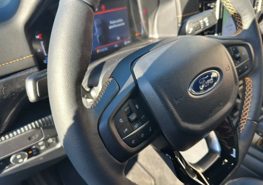 Gros plan sur le volant en cuir noir avec surpiqûres orange du Ford Ranger 2025, tableau de bord numérique en arrière-plan.