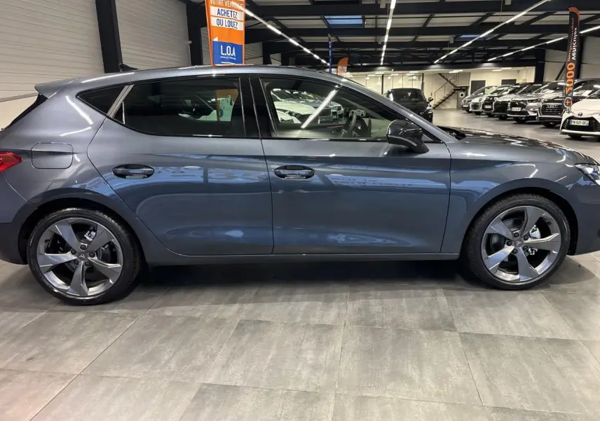 Vue de profil côté gauche d'une CUPRA Leon gris magnetic avec jantes alliage 18 pouces dans un showroom.